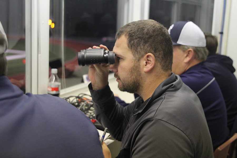 Looking through binoculars, announcer Nick Peirce tries to get a clearer look on players on the field for him to give details to the audience. 