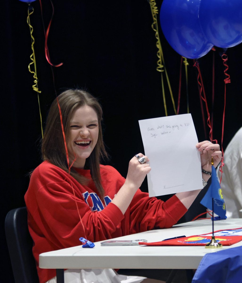 Laughing, senior Caroline Alley holds up her paper to sign.