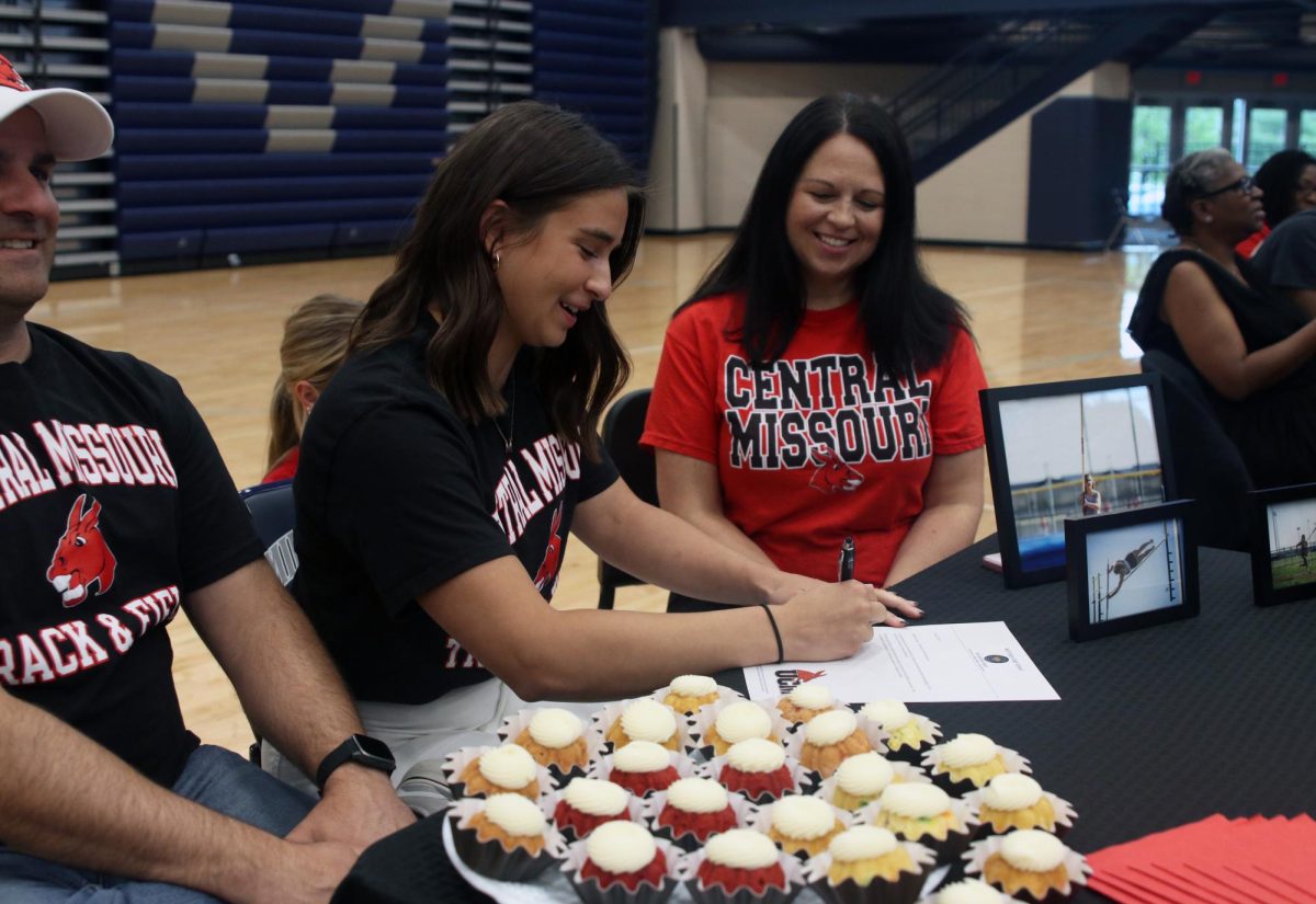 Smiling, senior Makenna Payne signs for Track and Field at University of Central Missouri.