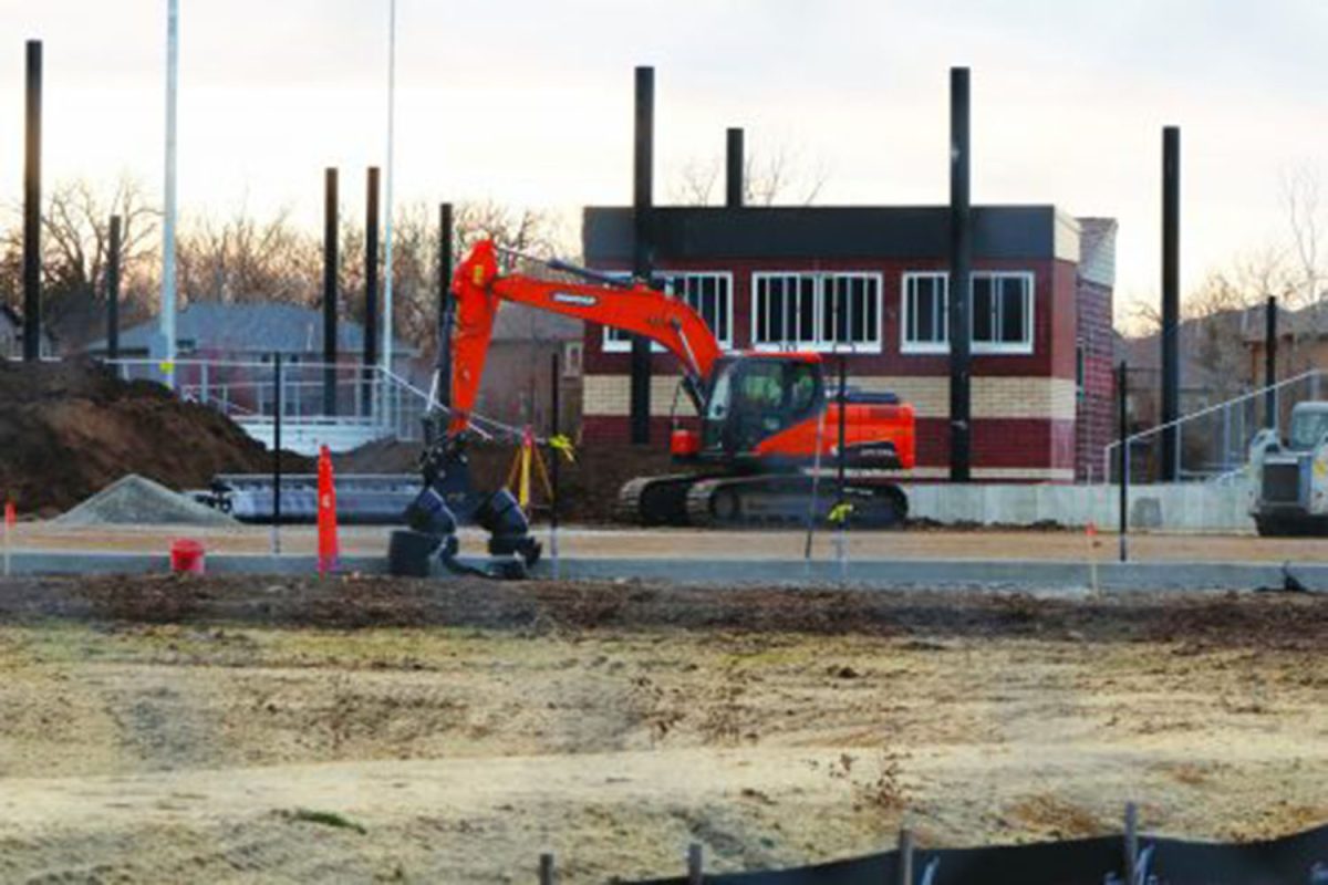 An excavator sits parked in front of the new softball press box and bleachers. The excavator was used to remove dirt in order to level the field so the future turf can be laid down December 2021. 