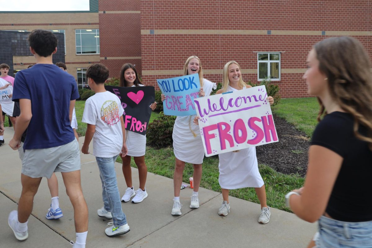 With smiles on their faces, seniors Calista Marx and Maggie Wieland hold up signs to welcome the freshmen.