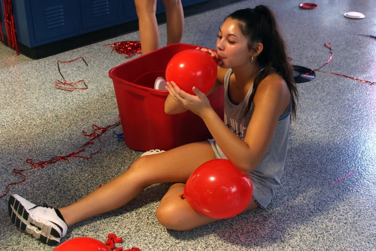 Sitting on the floor, junior Stella Beins blows up a balloon for the junior hallway.