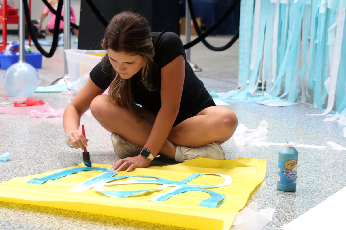 Sponge in hand, senior Brynn Shideler paints a “Mamma Mia!” themed sign. 