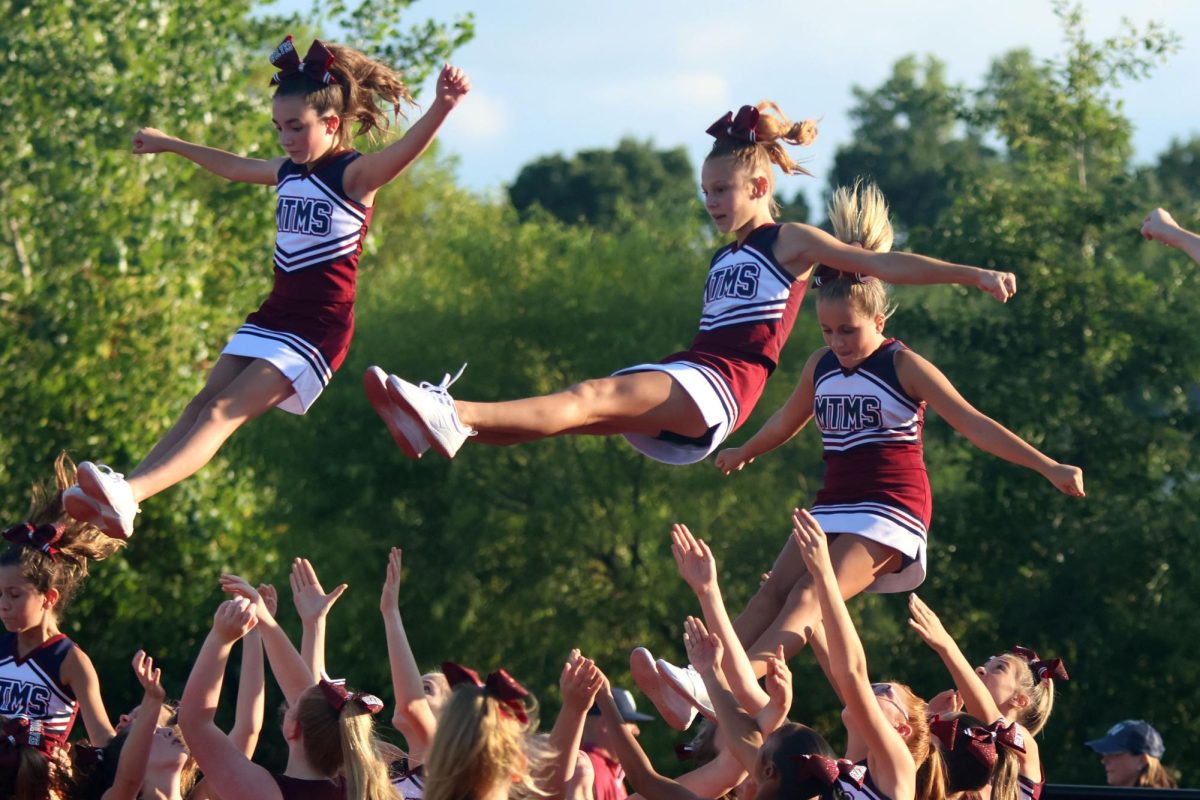 Middle school cheerleaders prepare to catch flyers after stunting.