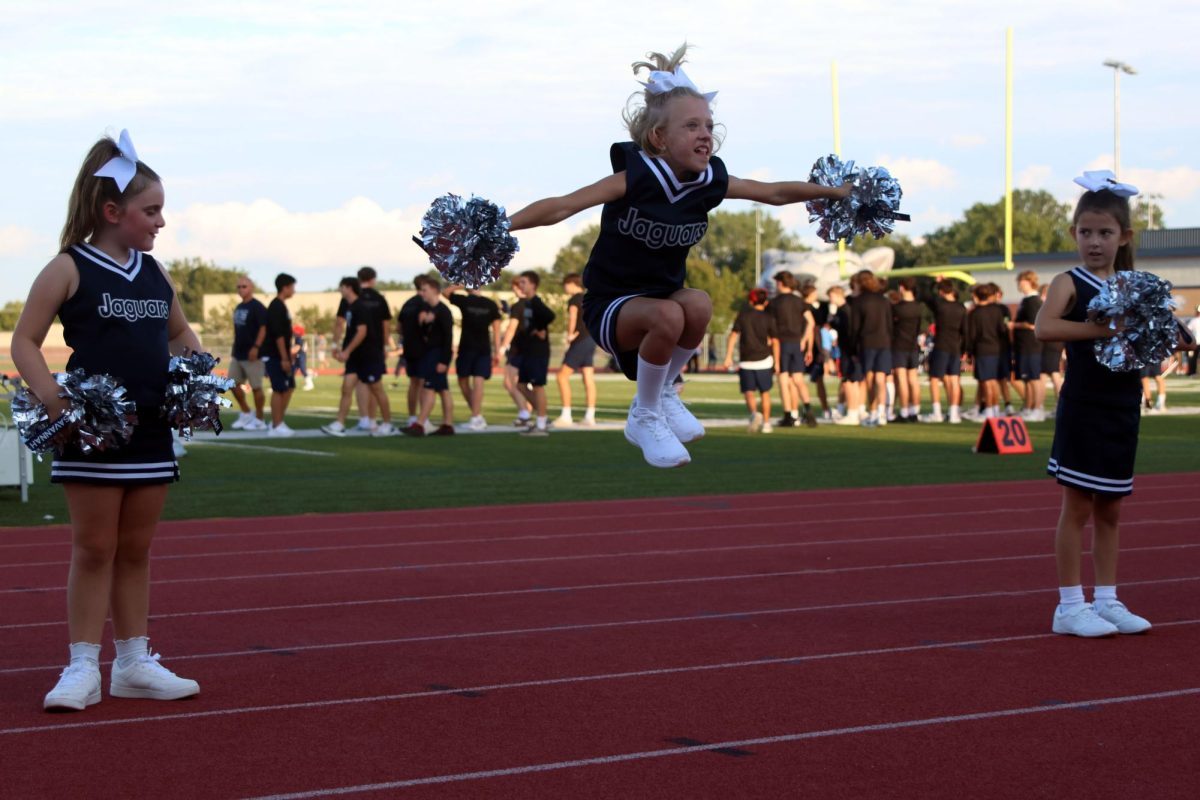 Junior Jag cheerleader performs her tuck jump while her teammates watch.