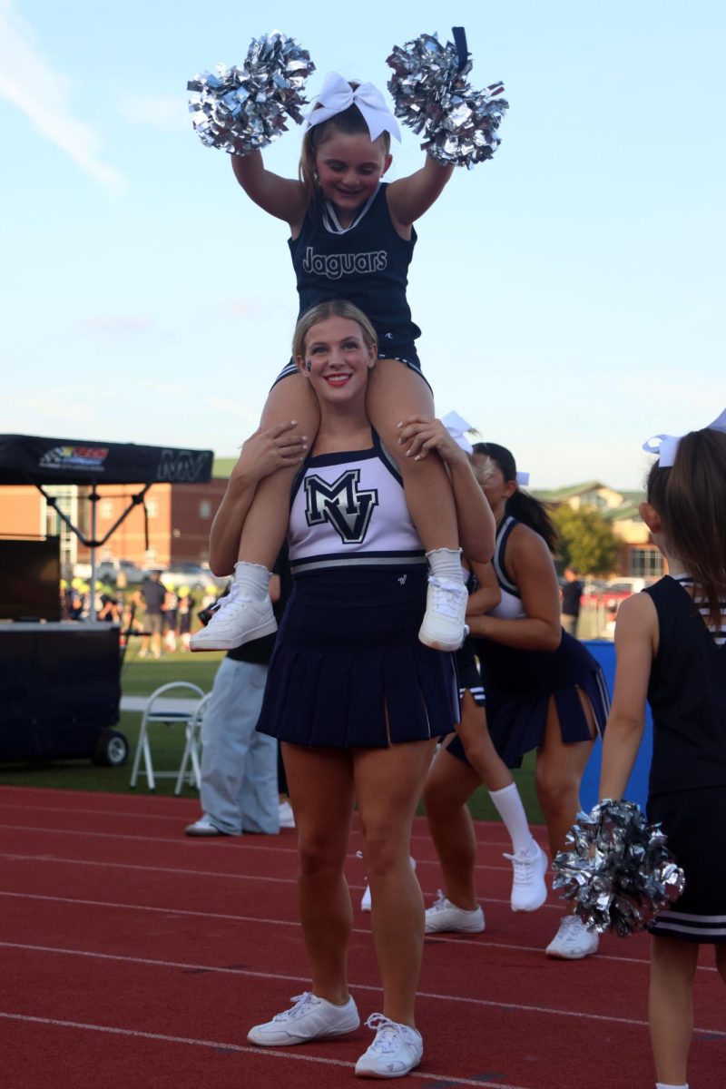 Senior cheerleader Reese Hartwick holds up Junior Jag cheerleader on her shoulders.