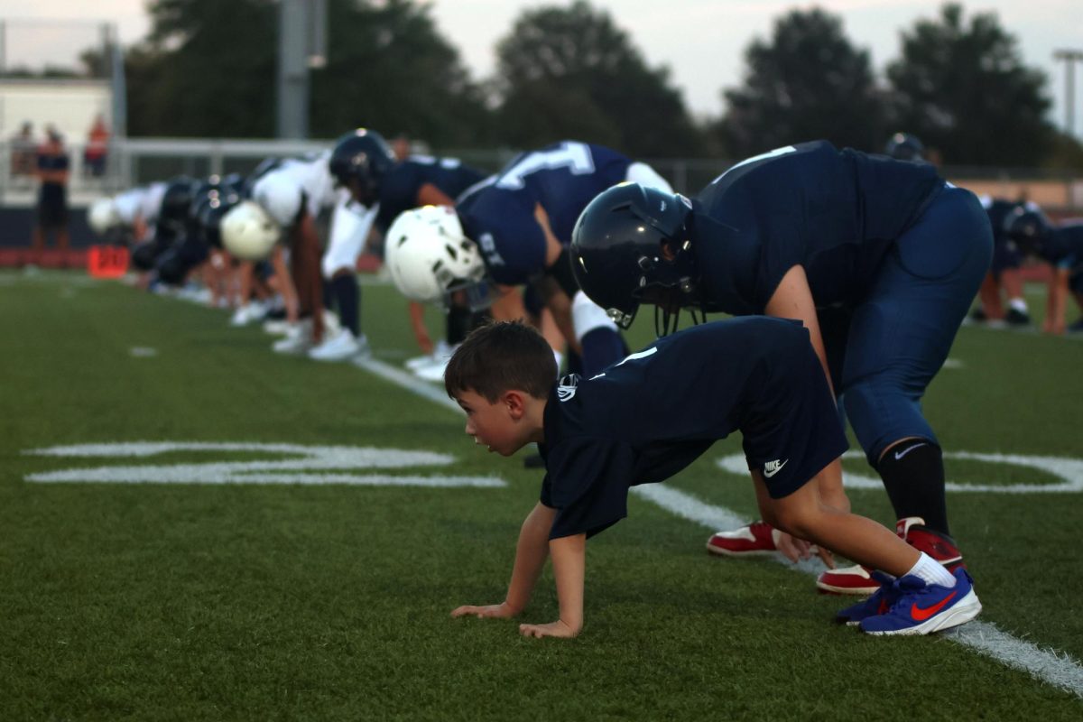 Child stretches along side high school football players.