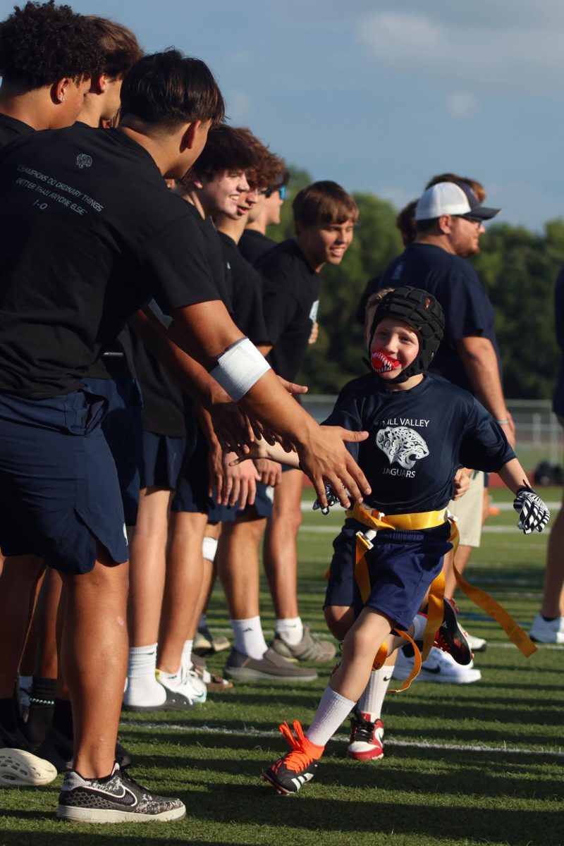 Smiling, Junior Jag football player gives high fives to high school football team members.