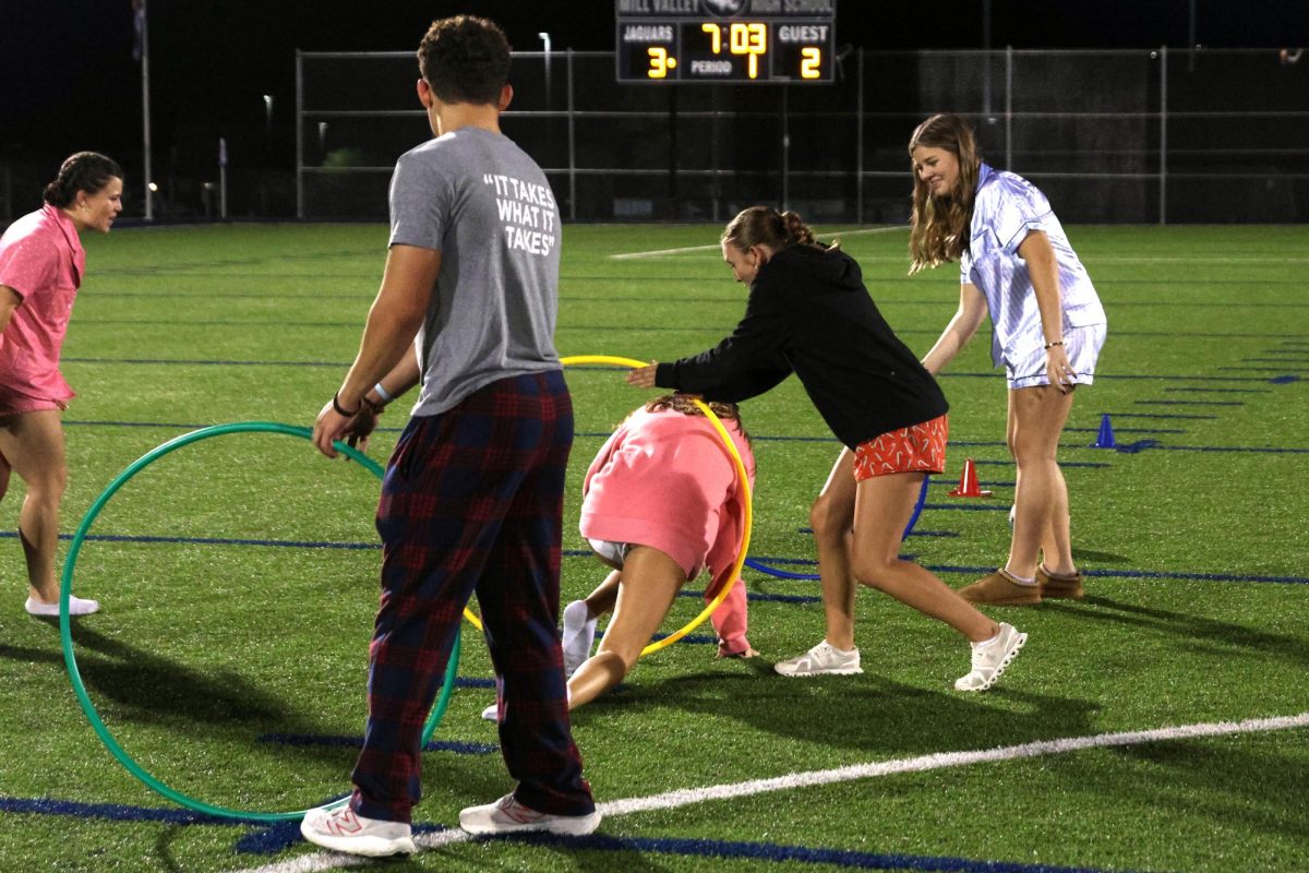 Juniors Max Bolan, Abby Heinisch and Ava Mendez hold up hoops as junior Callie Smouse crawls through during Jaguar Leadership Corps half time show at varsity soccer game Thursday Sept. 26.