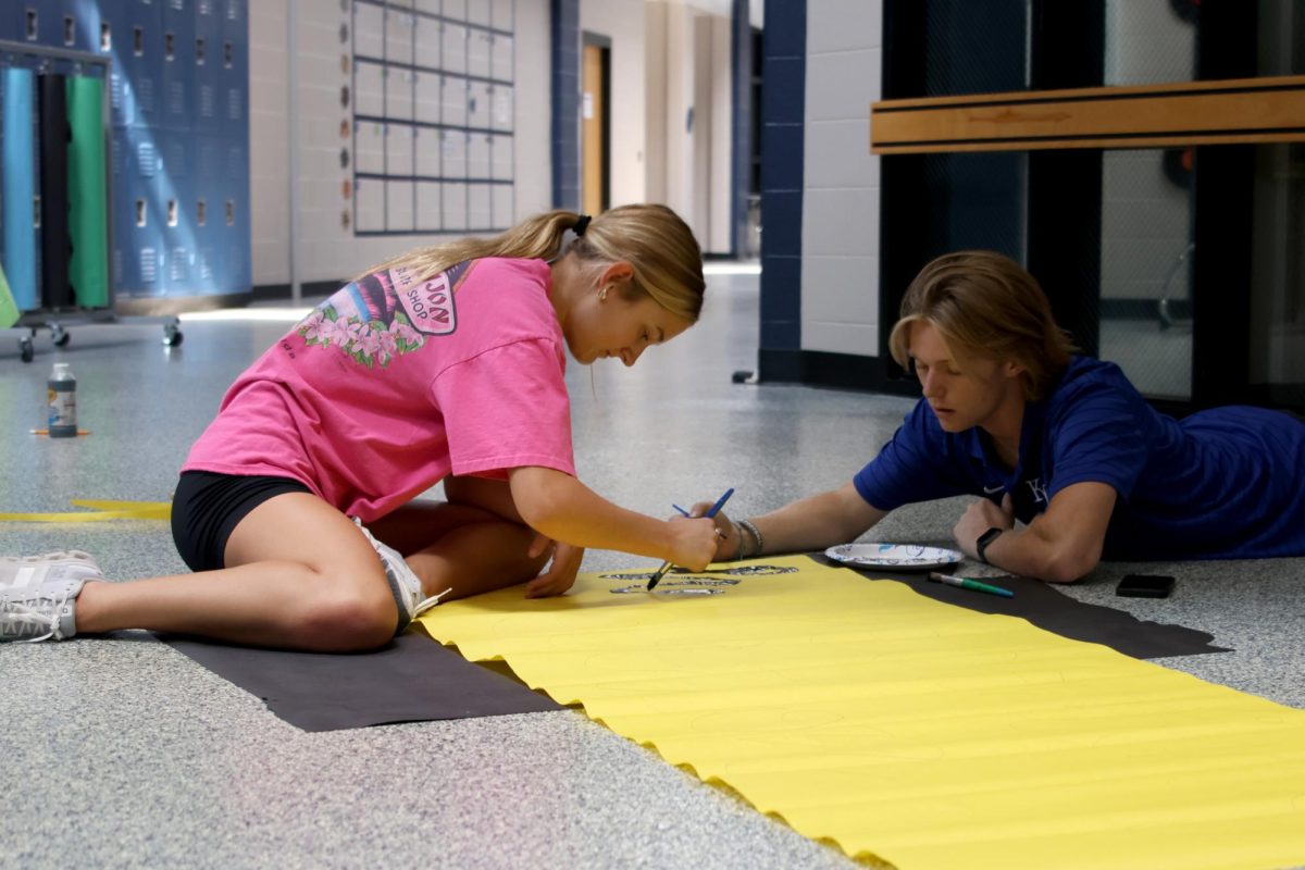 Working together, junior Mallory Lux and senior Clayton Sondgeroth paint a "homecoming edition" sign.