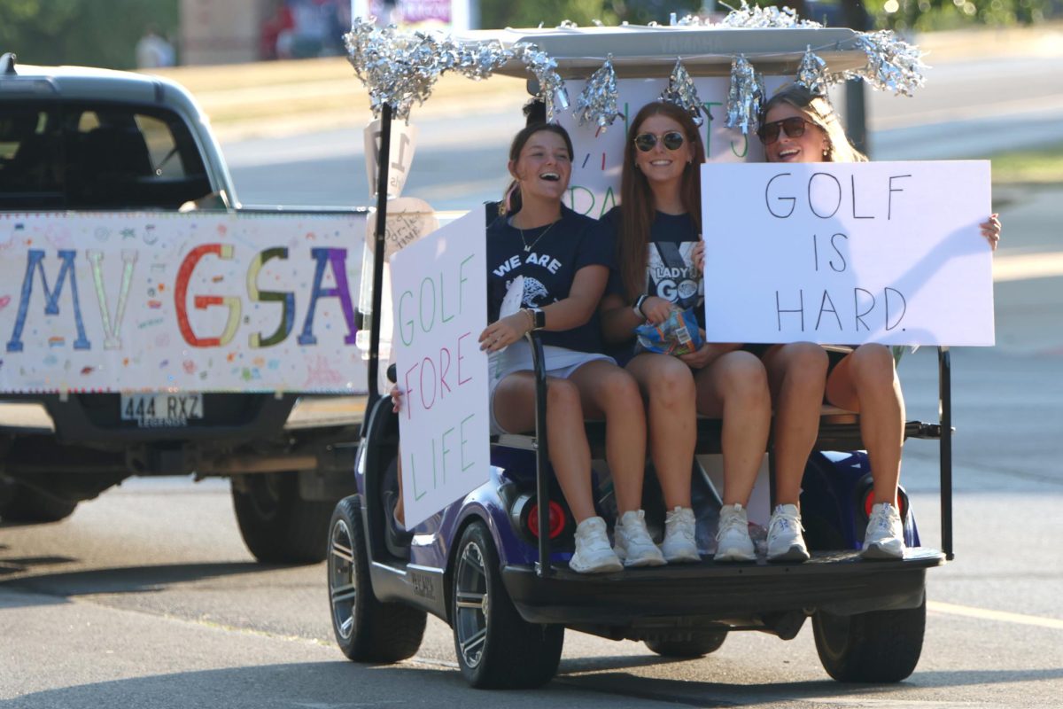 Holding up signs, juniors Maddie Martin, Sophie Van Inwegen and Lola Dumler ride a golf cart in the parade. 