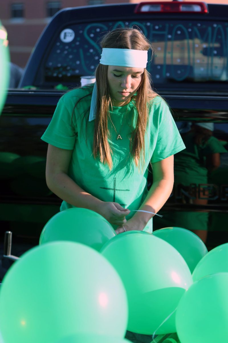 Adding finishing touches to the sophomore float, sophomore Avery Royer ties green balloons to the trailer. 