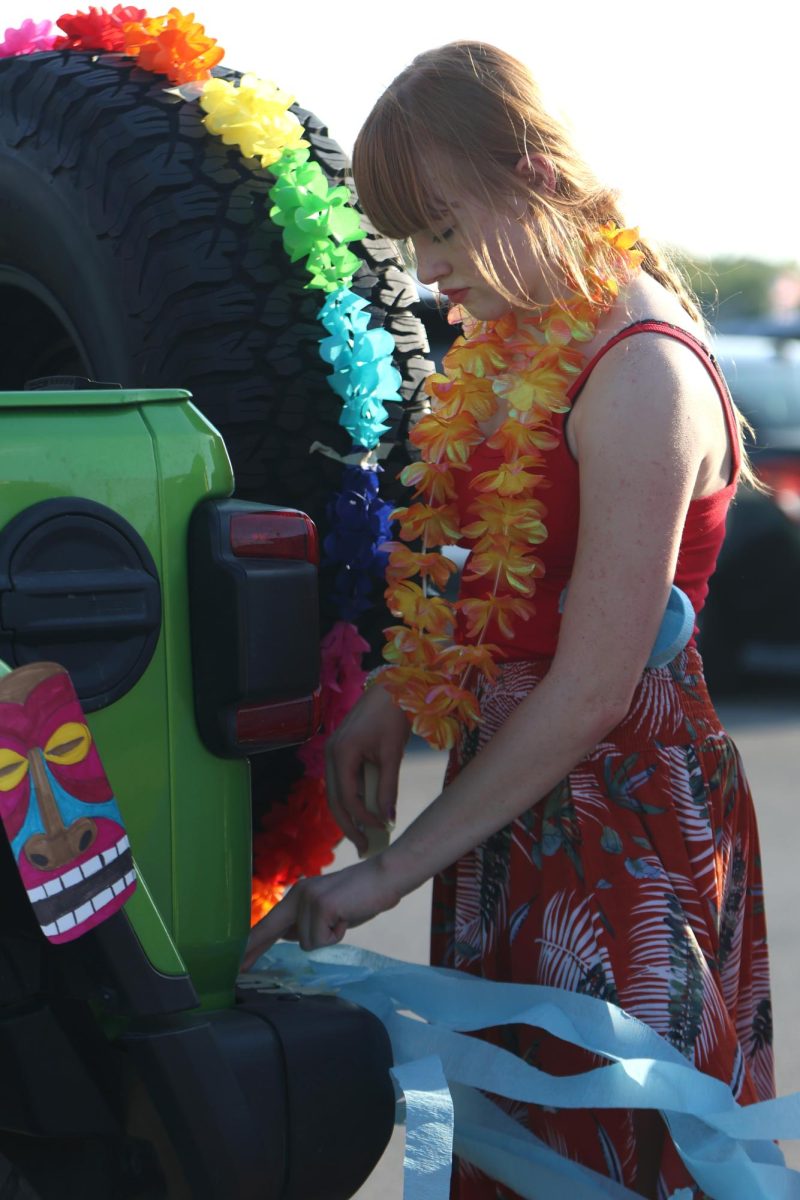 Taping up blue streamers, sophomore Lydia Reynolds contributes to the choir float. 
