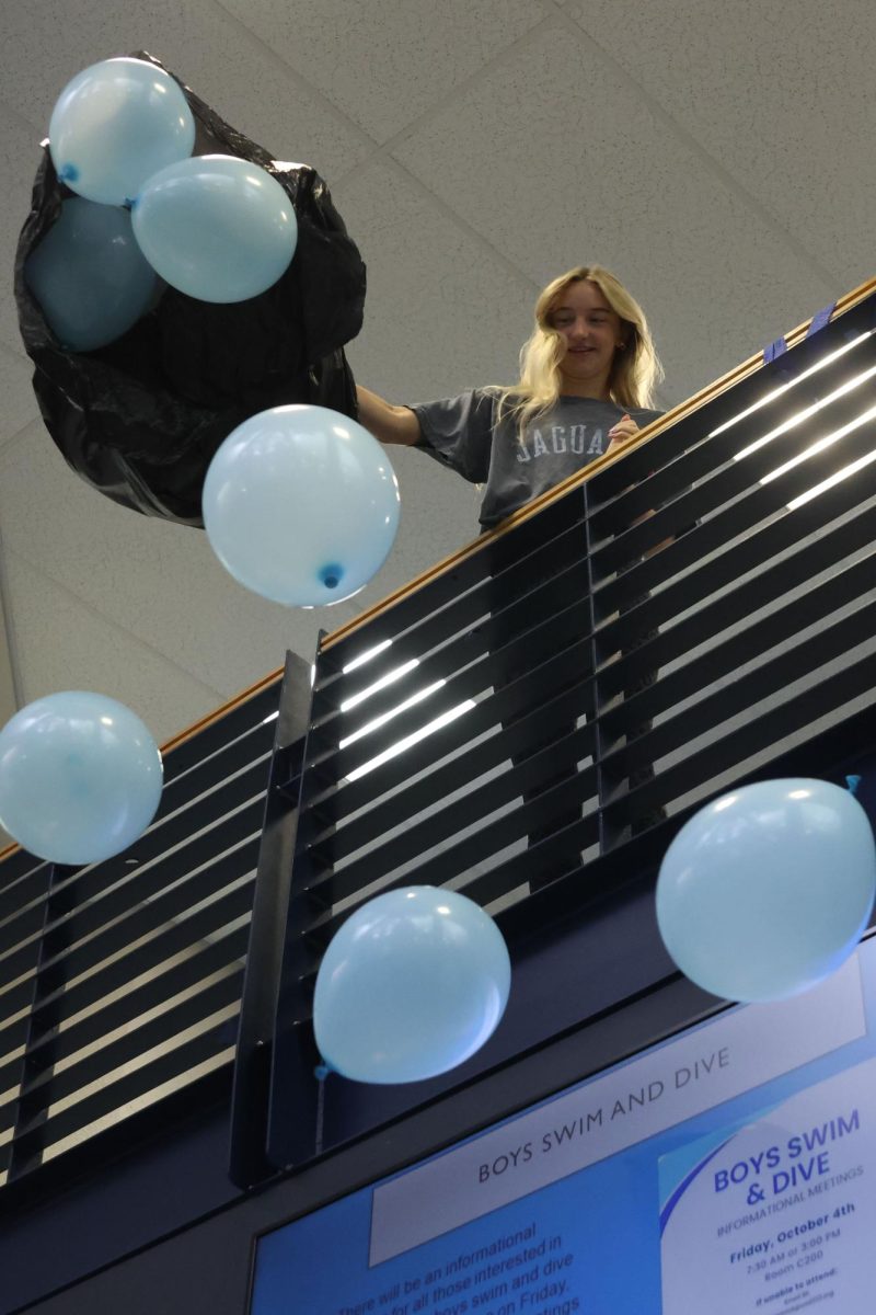 Looking down, senior Emma Mahoney dumps out a bag of blown up balloons onto the people below.
