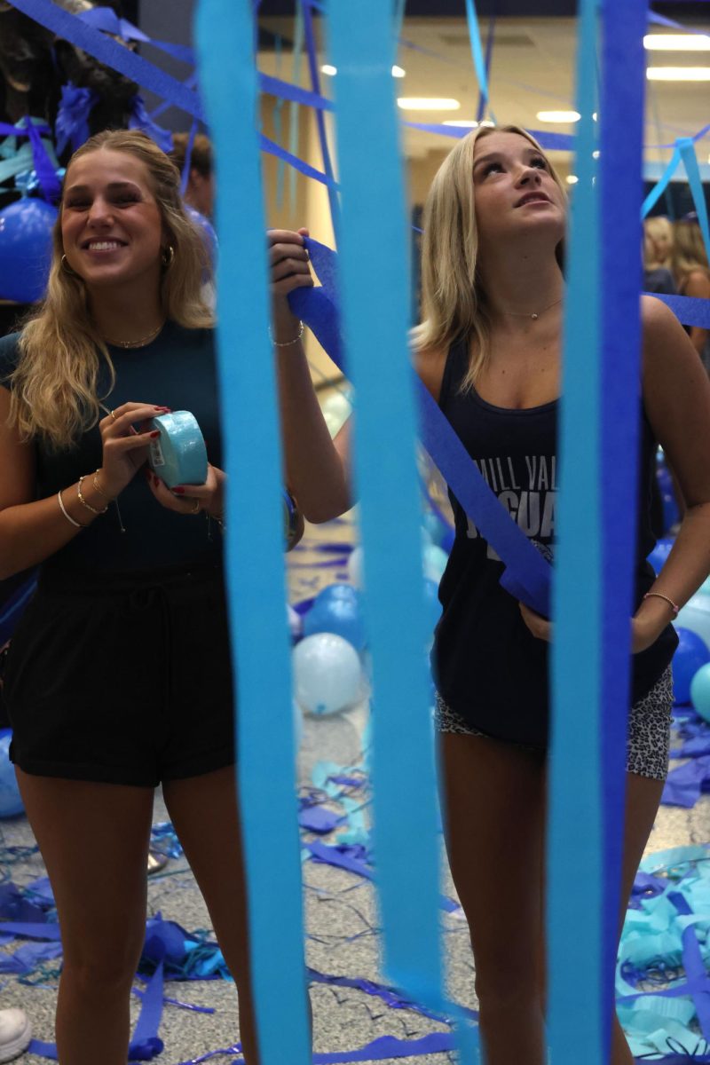 Smiling together, seniors Caroline Hooper and Mia Modrcin hang up streamers around the entry.
