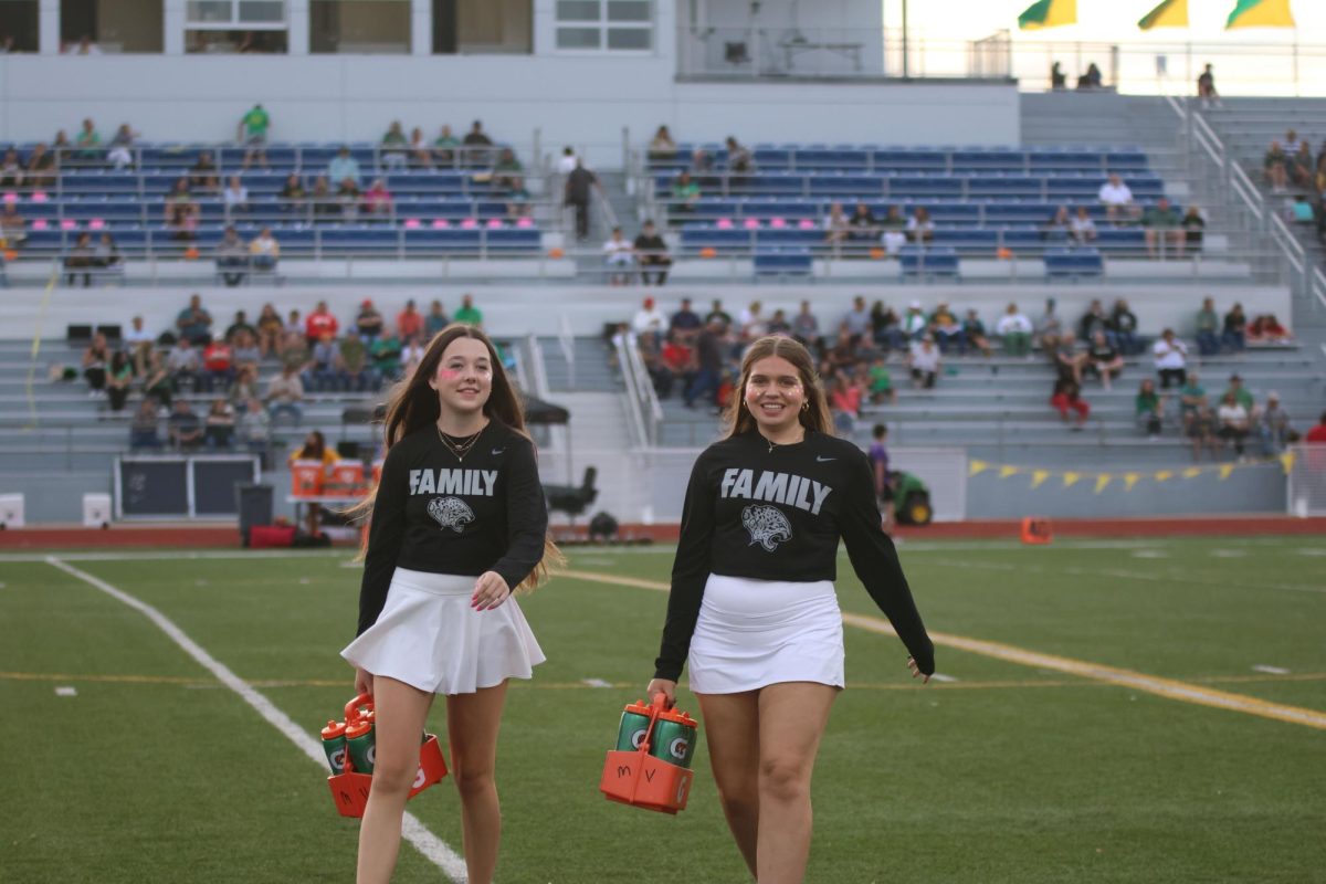 Smiling at the camera, junior Abby Allen and sophomore Cassidy Stuke bring water over to the players.