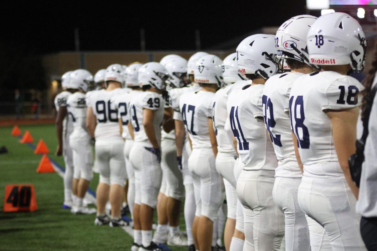 While watching the game, the football team stands on the sideline.