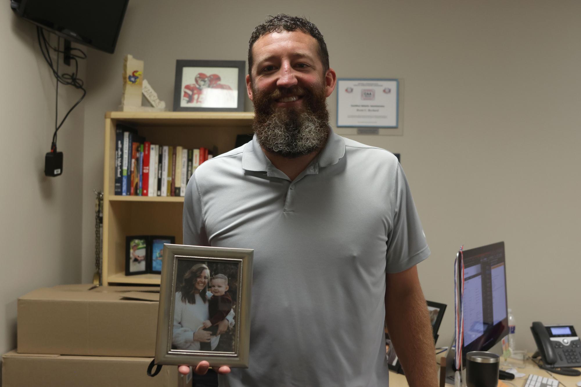 Athletic Director Brent Bechard stands in his office with a picture of his family that is important to him.