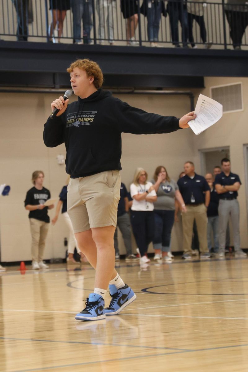 Microphone in hand, senior Aiden Lehr announces at the Homecoming pep assembly.