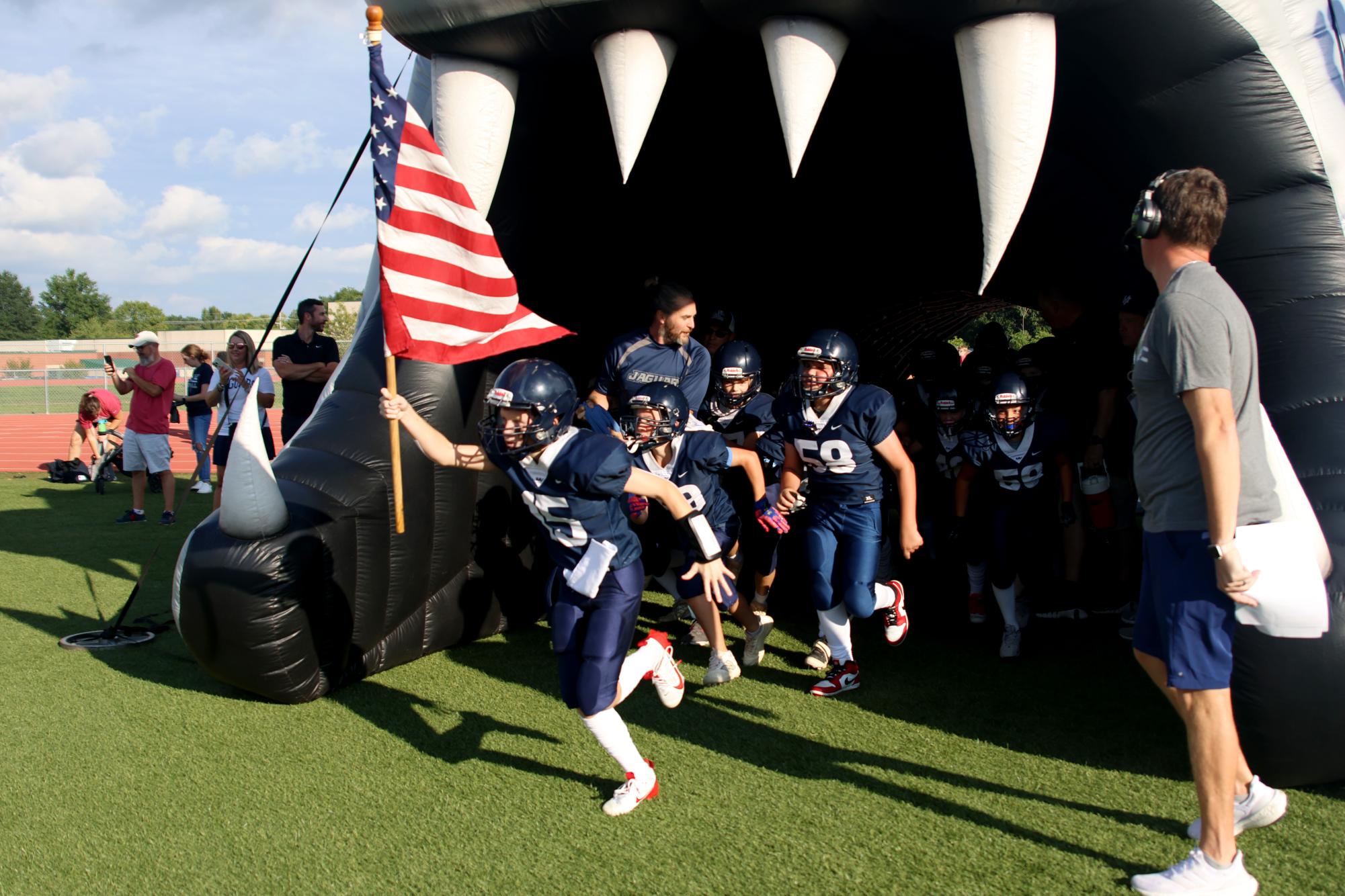 Beginning to run out, Junior Jag football players run out with an American flag.