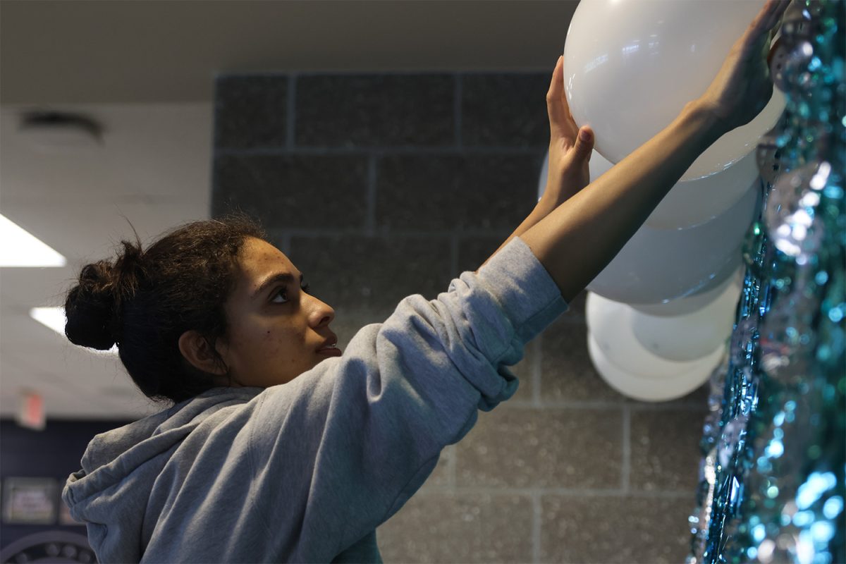 Preparing the backdrop for the entrance of the dance, Senior Kenzie Johnson carefully places balloons over the top of the concession stands.