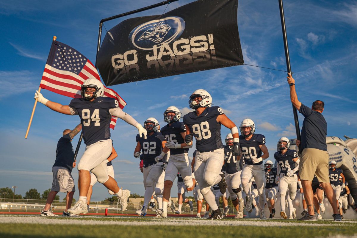 Running out of the jag head, junior Hayden Heller leads his team with the American flag.