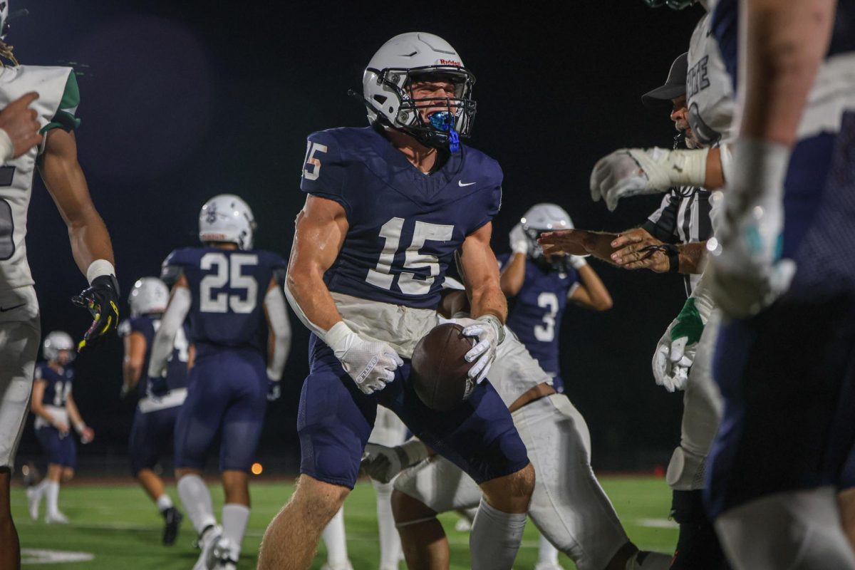 Flexing, senior Andrew Watts celebrates with the team on the sideline after a catch.