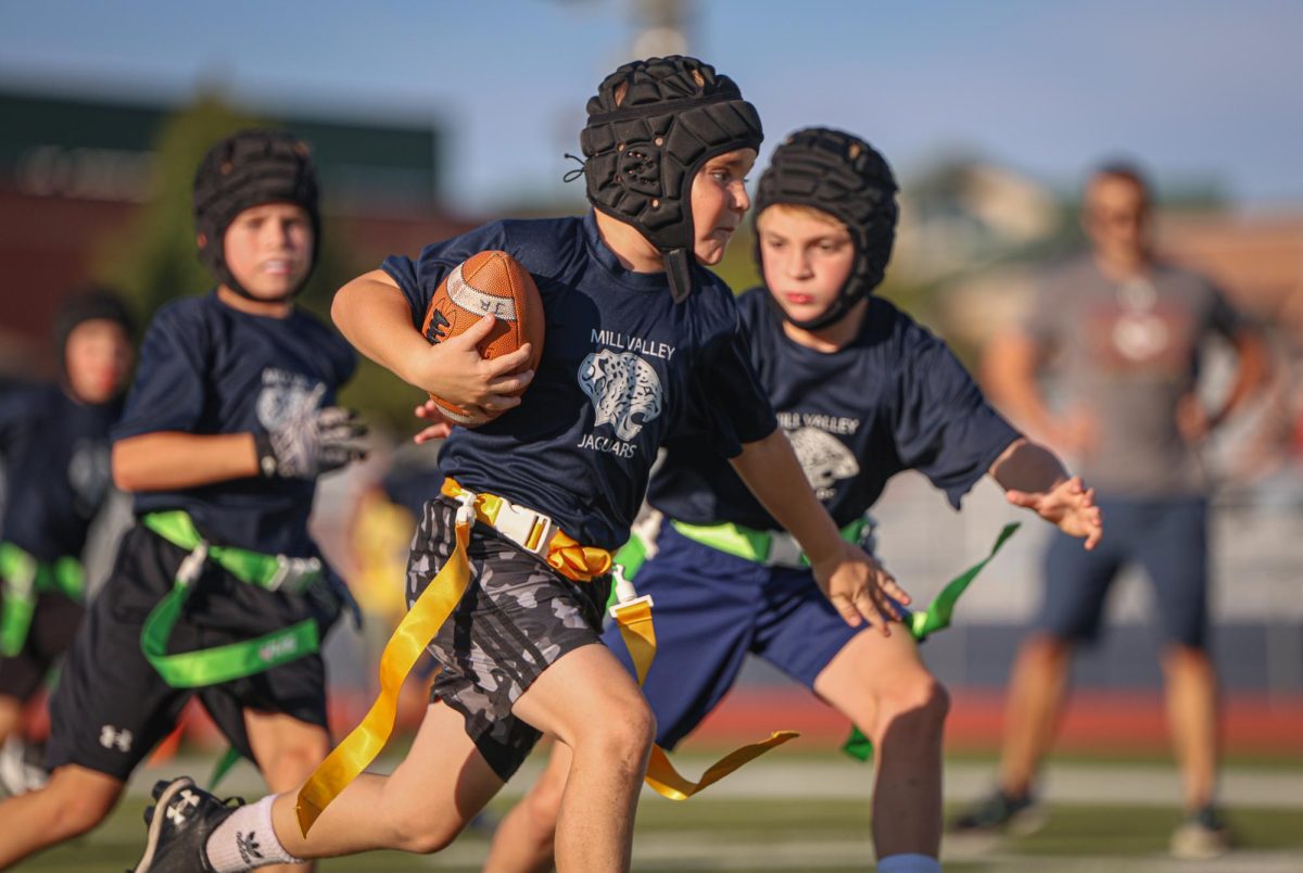 Holding the ball tight, a Junior Jag football player runs upfield to avoid getting his flag pulled.