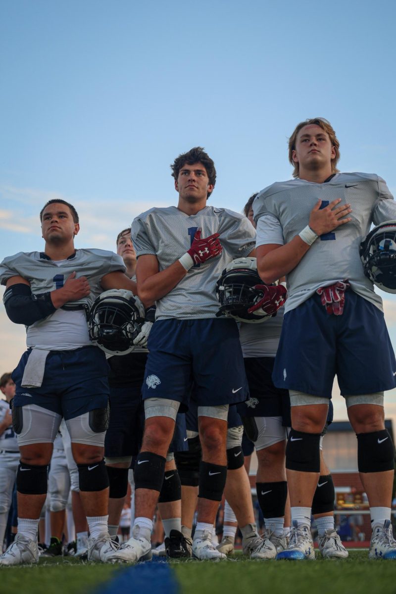 With their hands on their hearts, seniors Zach Zaldivar, Isaac Sauder, and Brody Brigham stand for the national anthem.