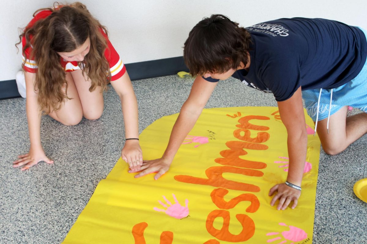 Freshman Ava Munsey helps Freshman Stewart Lovejoy put his handprint on the freshmen poster. 
