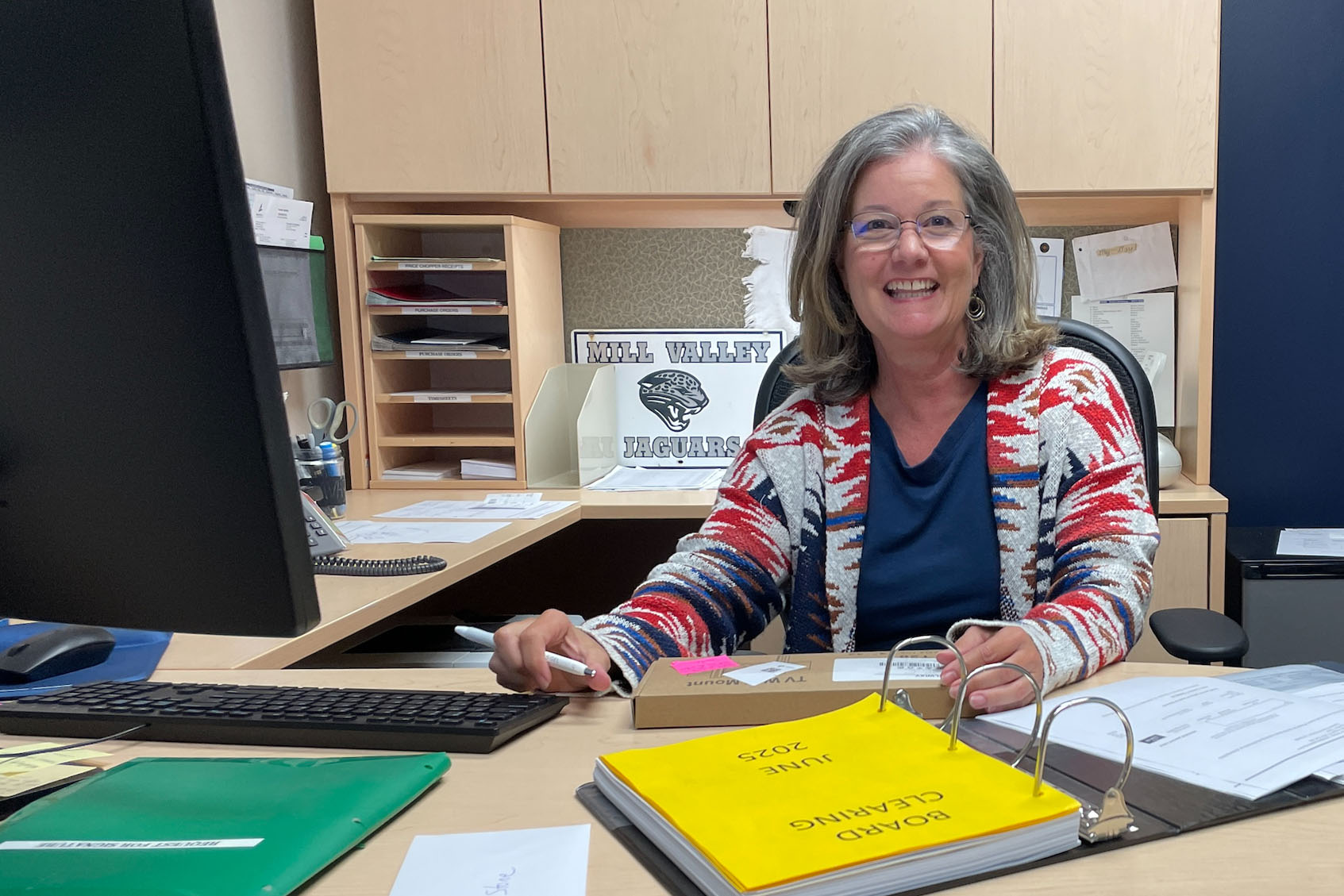 Bookkeeper Darlene Deas sits at her desk in front of her original Mill Valley sign in her office while working on bills and keeping financial records for the school