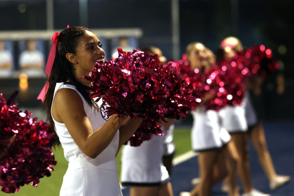 Poms up, senior Kenzie Johnson cheers to the student section.