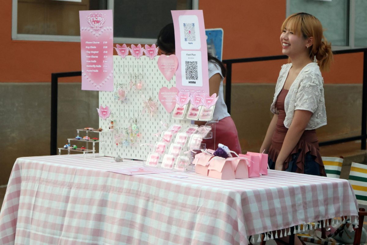 Girl smiles as she converses with a customer at her table selling nails, charms and magnets.