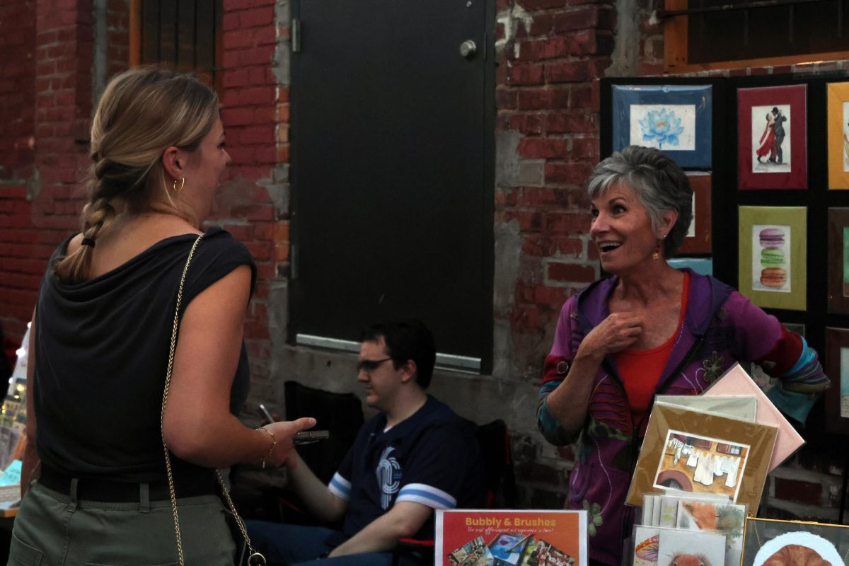 Artist selling her art laughs as she converses with First Fridays attendee.