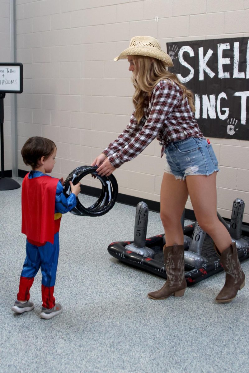 Running the Skelton Ring Toss booth, sophomore Avery Huber hands the rings to a Haunted Halls participant. 