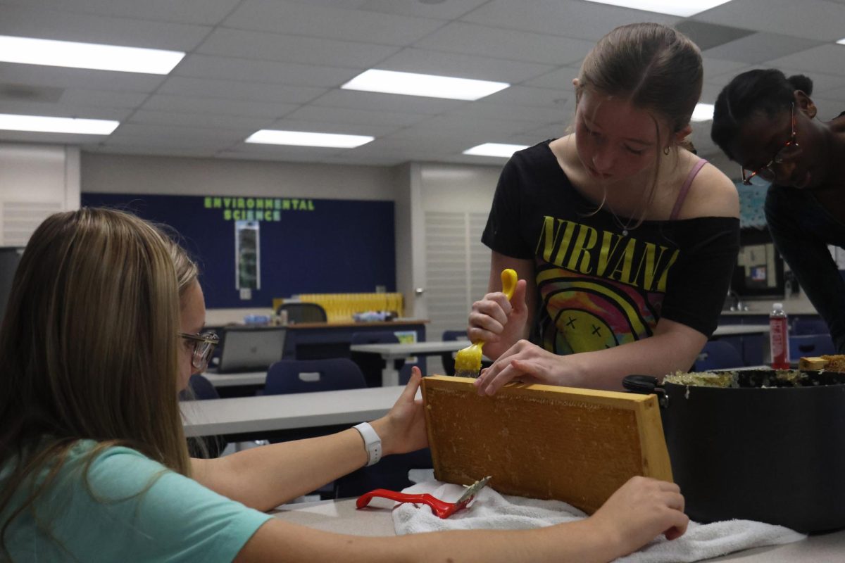 Senior Marissa Akehurst supports the frame for Senior Cadence Kerr as she scrapes off the wax. 