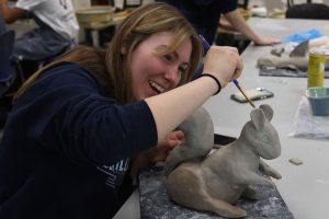 Senior Piper Wendler laughs as she smooths out her sculpted squirrel for ceramics.