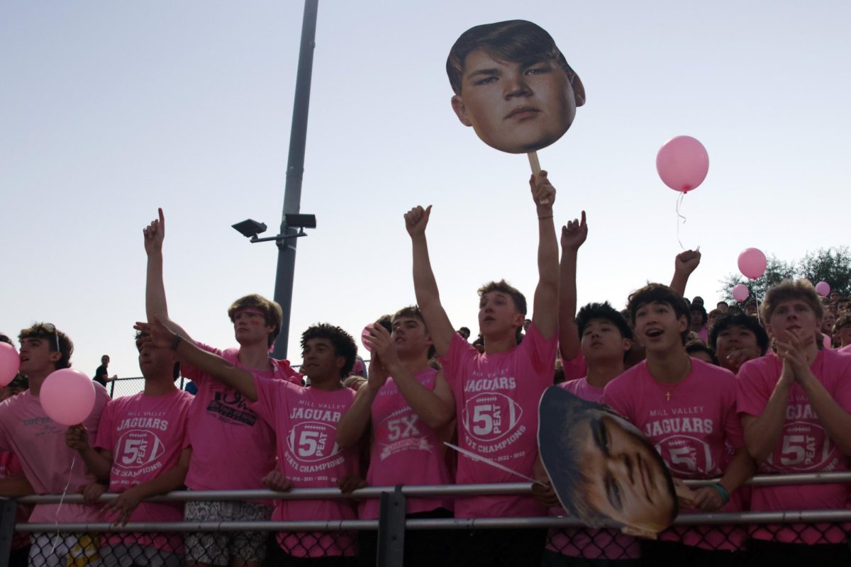 At kickoff, senior Hudson Powers holds a cutout of senior Eric Penner while cheering along with his friends.
