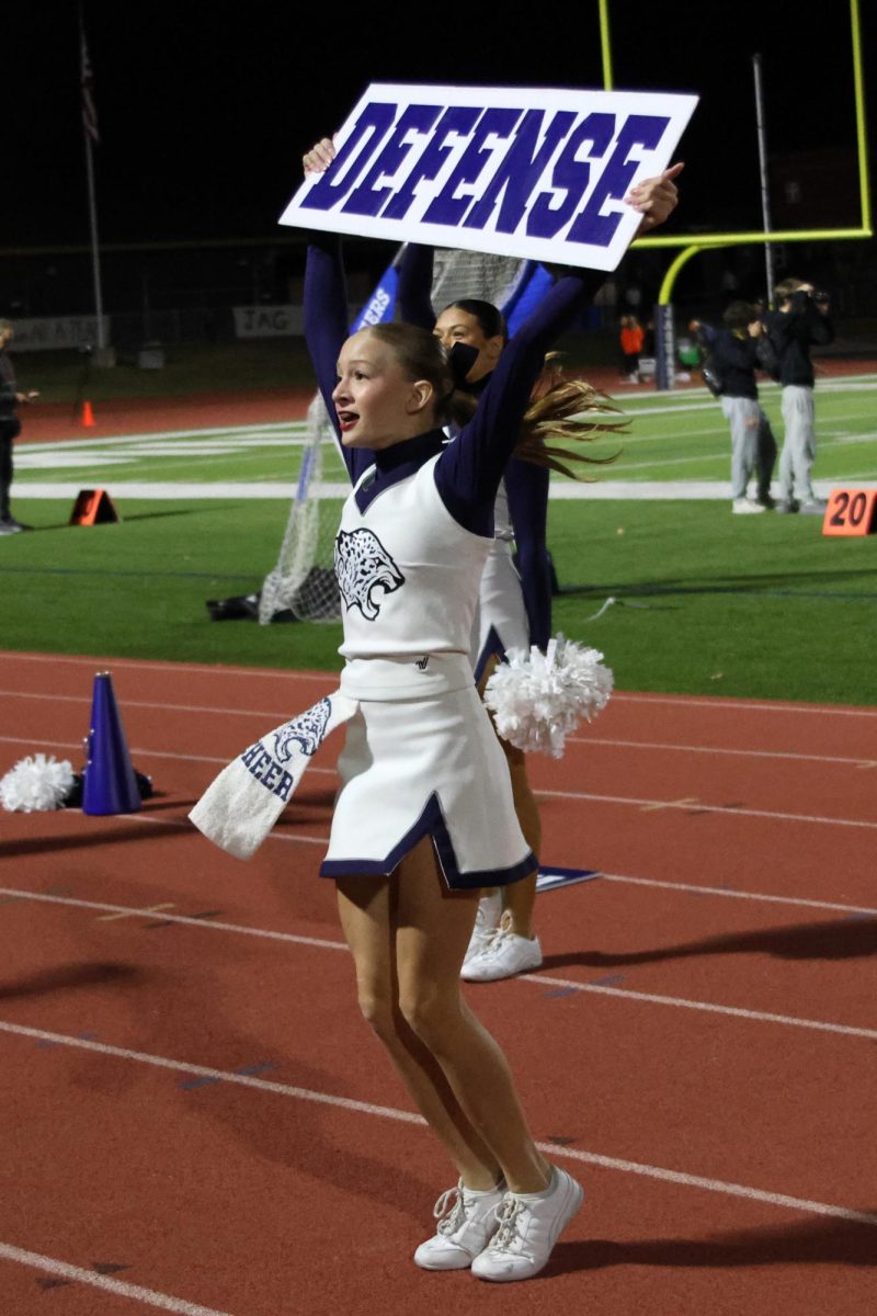 Freshman Isabella Herman pumps up the crowd with a defense cheer alongside her teammates on the JV Cheer team.