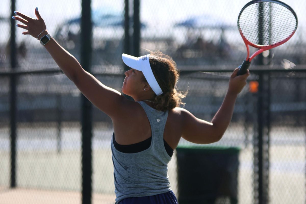 Racket in the air, senior Kyra Nelson gets ready to serve the ball to her opponent. 


