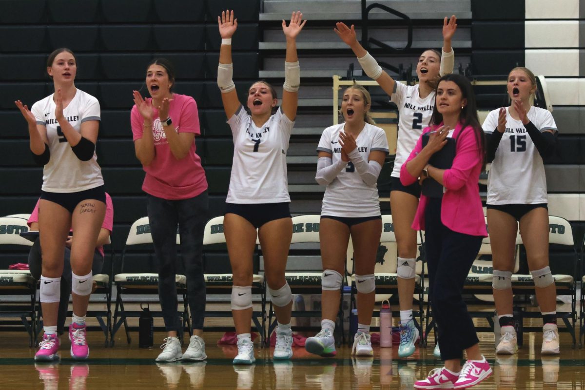 After winning the point, the girls on the sideline celebrate and cheer for their teammates. 