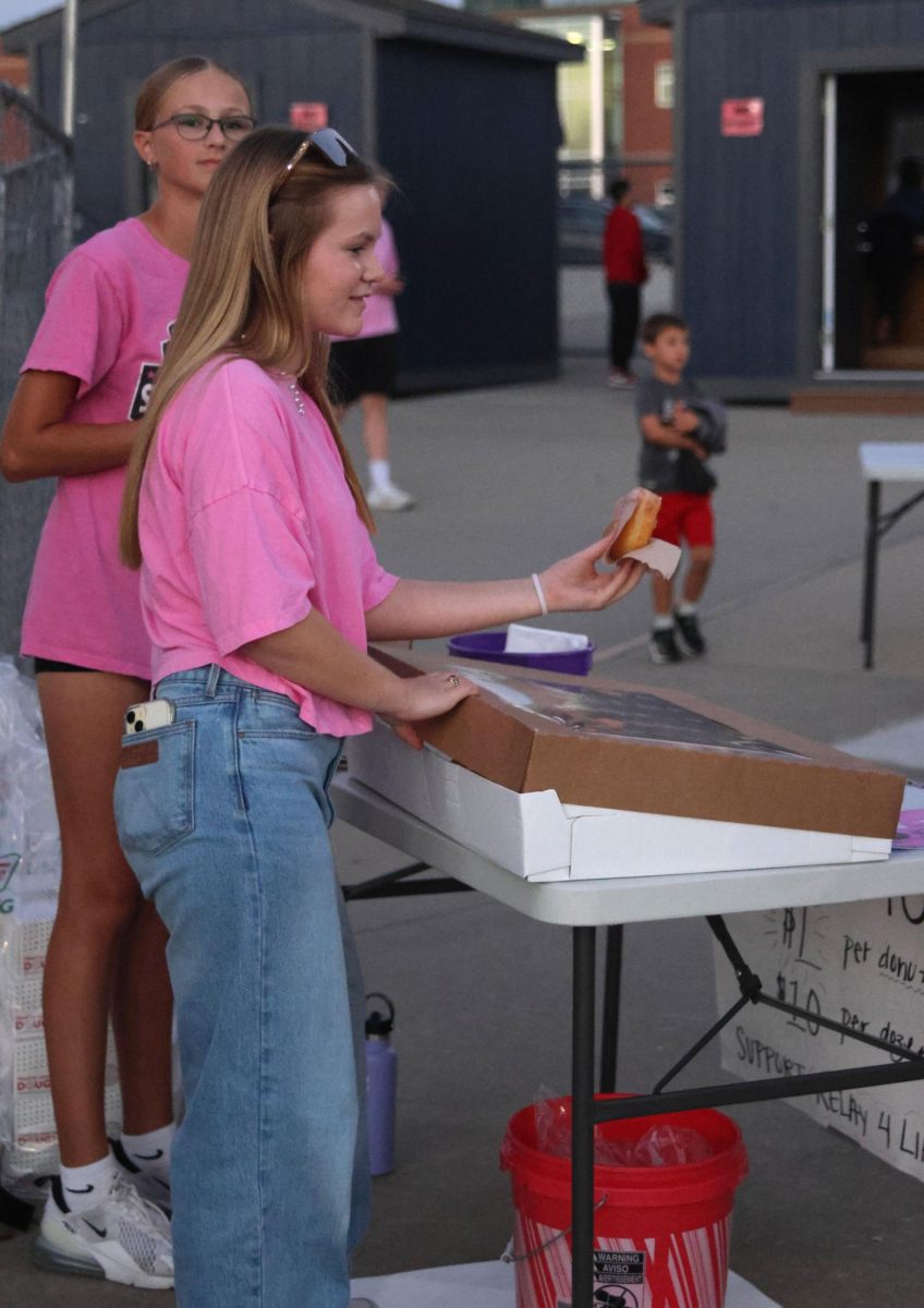 With her hand out, freshman Paige Lowe gives a little kid a donut. 