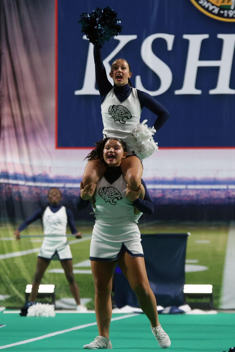 On junior Ava Lucht’s shoulders, junior Lilli Verbenec raises a pom in the air.