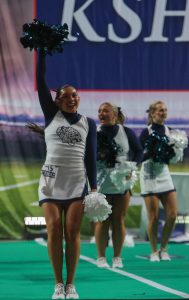 Smiling, junior Stella Beins waves her pom poms in the air.
