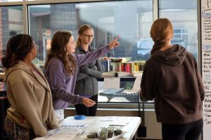 Pointing to the board, freshman Ava Munsey explains the prices at the entrance. 