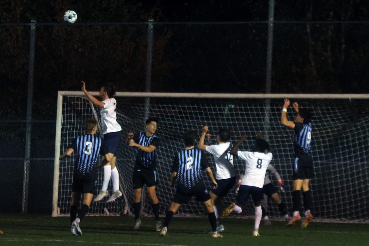 Players jump to header the ball coming towards the goal from a corner kick. 