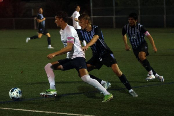 Senior team caption Nic Schrag dribbles the ball while being closely followed by defender. 