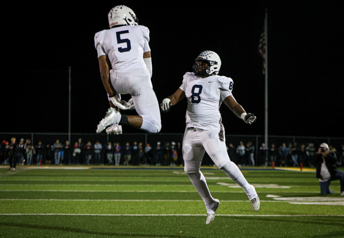 With his hands between his legs, senior Jayden Woods jumps to high five senior El-Roi Hasabu.