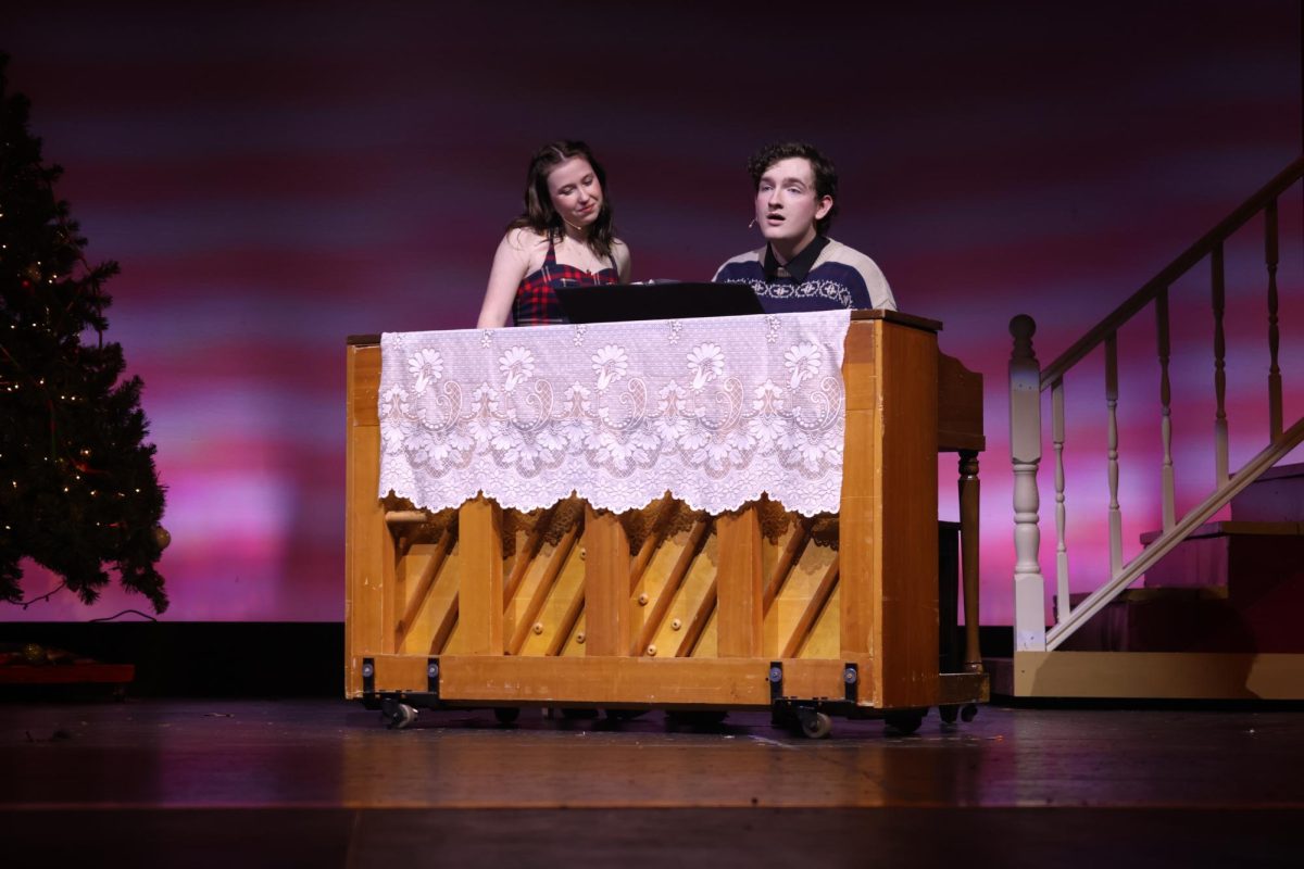 Playing the piano, senior Blake Gray sings a song his character wrote while senior Reese Miller admires the music, Monday, Dec.2.