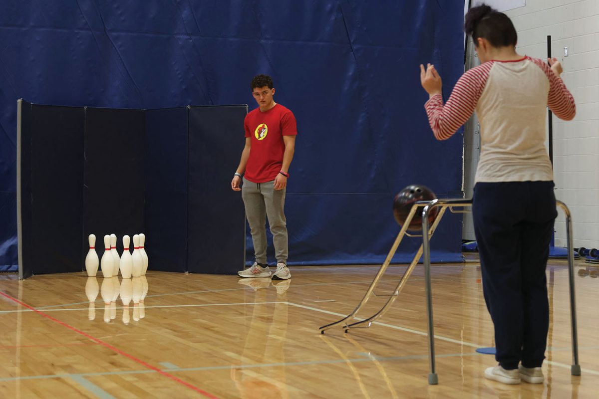 Helping his peer, junior Max Bolan helps out with the bowling unit in unified PE, Wednesday Nov. 13.
